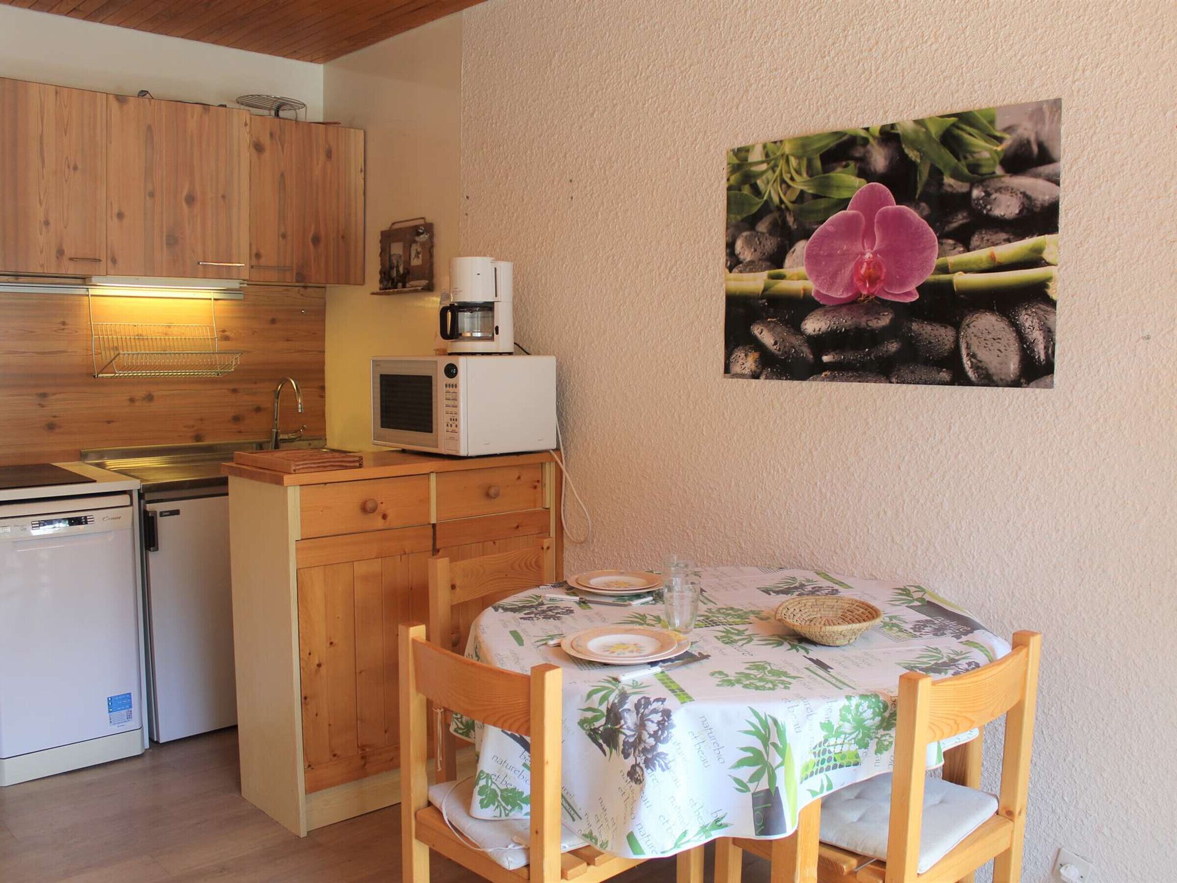 A compact kitchen with wooden cabinets, a microwave, a coffee maker, and a dining area with a table set for two.