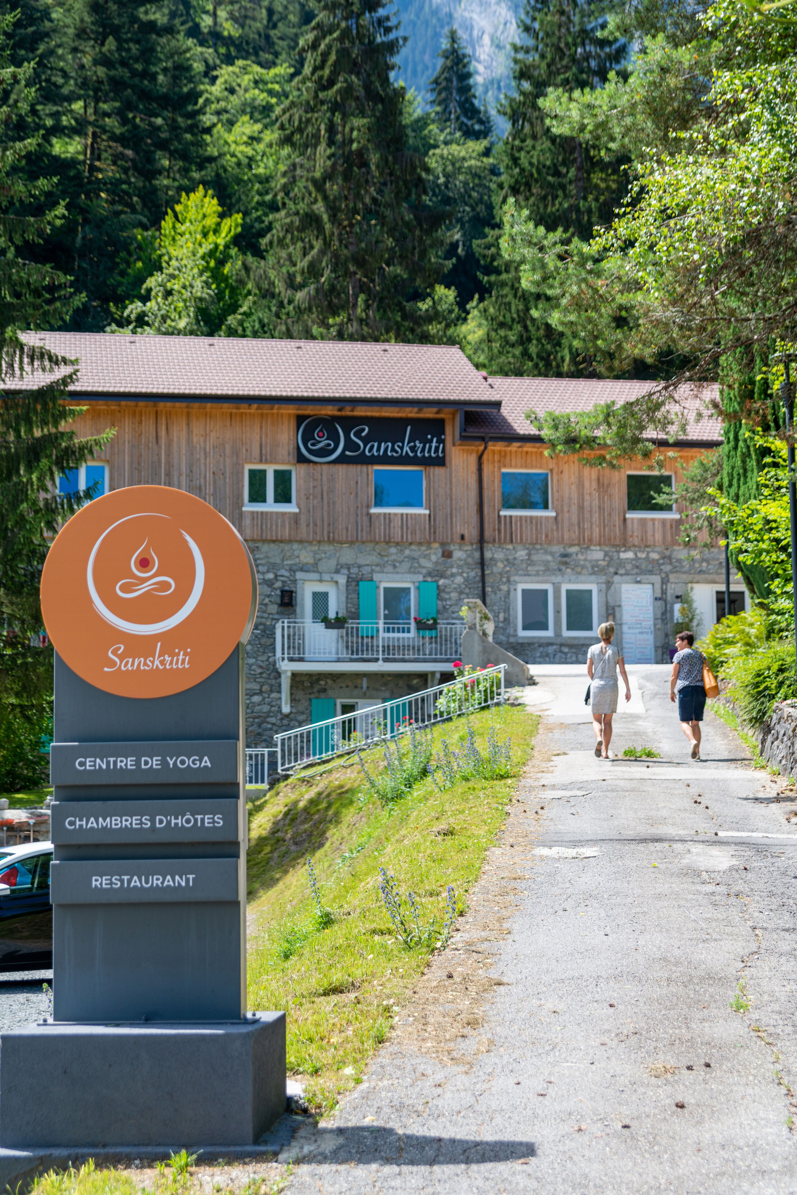 A sign for a yoga center, hotel, and restaurant with a mountainous backdrop.