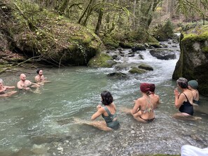 Een groep mensen in een natuurlijke omgeving, met een stromende rivier, omringd door bomen en rotsen.