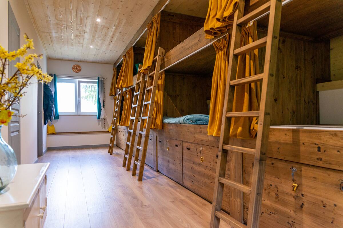 Een houten blokhut van binnen met stapelbedden, een raam met gordijnen en een houten dressoir.