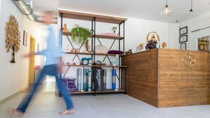 A modern reception area with a wooden reception desk, metal shelving with various items, and a visible ductwork on the wall. - Chambres d'Hôtes Sanskriti (Scionzier)