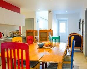 Een eetgedeelte met een houten tafel, kleurrijke stoelen en een keuken op de achtergrond.