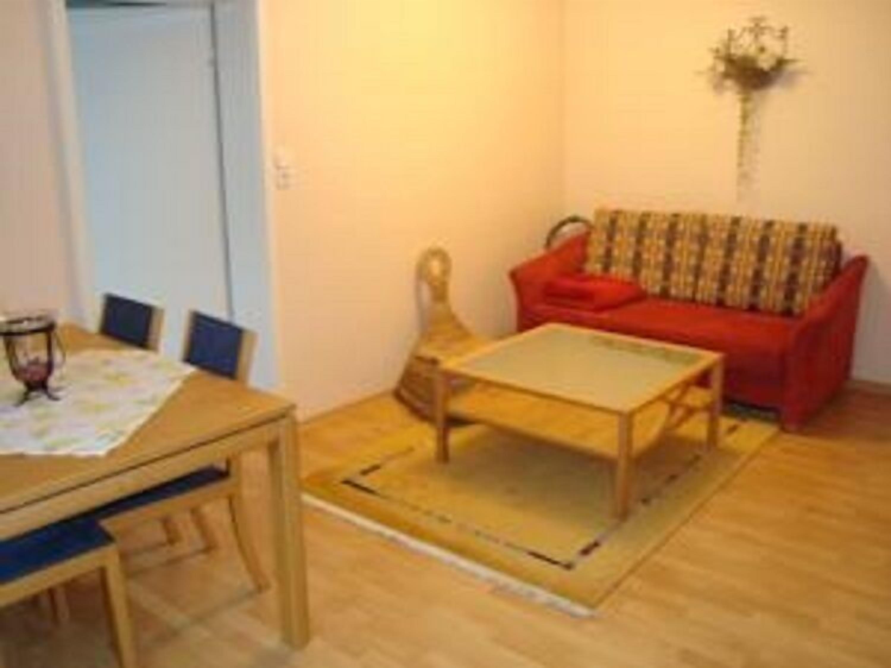 Una sala pequeña con una mesa de madera, un sofá rojo y una planta decorativa.