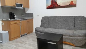 Un espacio habitable pequeño con kitchenette, sofá gris y una mesa de centro negra.
