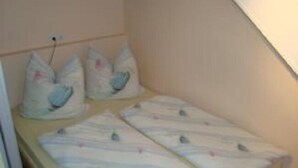 Una habitación pequeña con cama individual, techo inclinado y cabecera de madera. En la cama, hay dos almohadas con diseño de p ájaros.