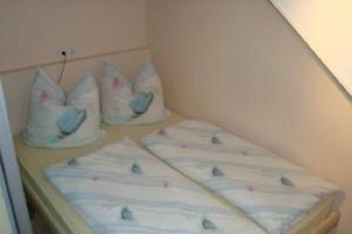 Une petite chambre avec un lit simple, un plafond en pente et une tête de lit en bois. Il y a deux oreillers à motifs d’oiseaux sur le lit.