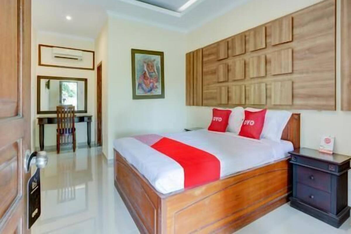 Un dormitorio con cabecera de madera, cama con ropa de cama roja y blanca, una mesita de noche y un escritorio con una silla.