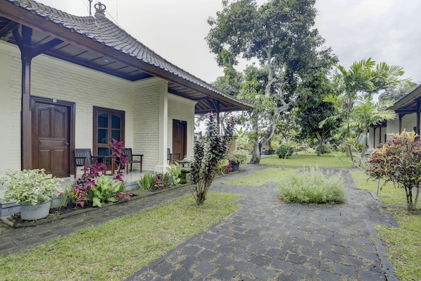 A traditional house with a tiled roof, a porch with chairs, and a garden with various plants.