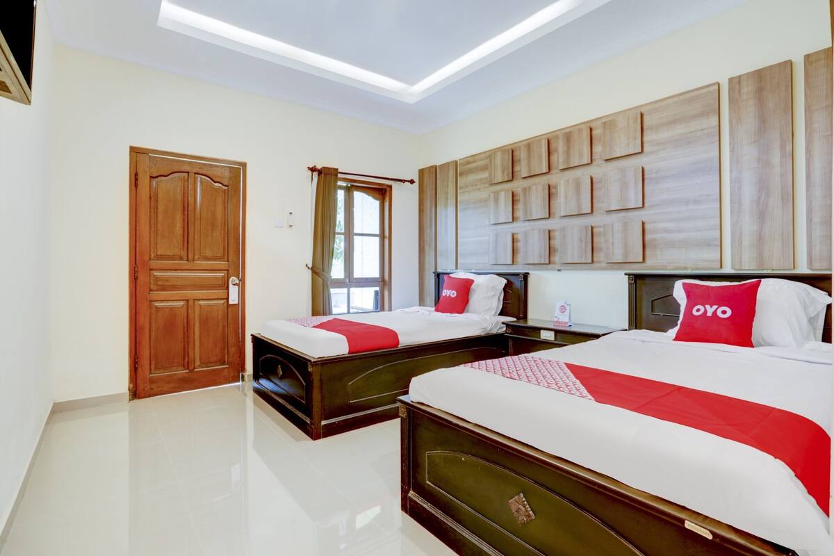 Una habitación de hotel con dos camas, una puerta de madera, una ventana con cortinas y una obra de arte colgada en la pared.