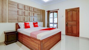 A bedroom with a wooden bed, a nightstand, a large window with curtains, and a wooden door. - Hotel O Astiti Graha Tanah Lot (Tabanan)