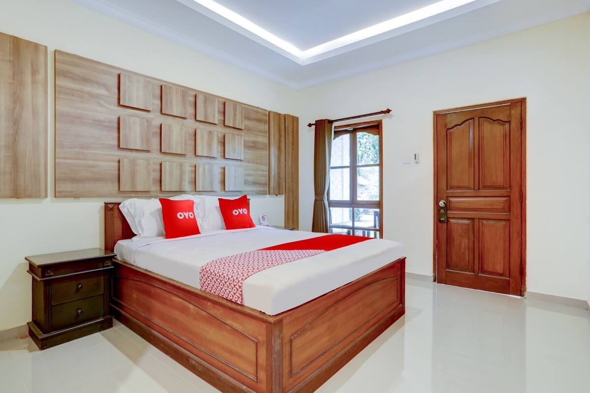 Un dormitorio con una cama de madera, una mesita de noche, un ventanal con cortinas y una puerta de madera.