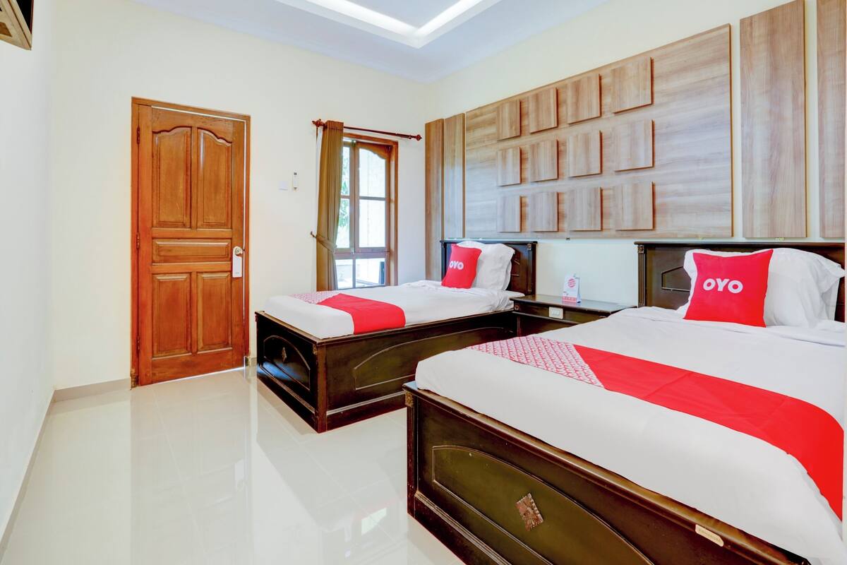 Habitación de hotel con dos camas, cabeceros de madera, un ventanal grande y una lámpara de techo.