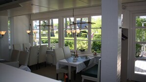 Un comedor con una mesa dispuesta para dos, paredes blancas y ventanas amplias que ofrecen vistas al verdor exterior.