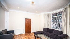 A living room with a dark-colored sectional sofa, a glass coffee table, and a wooden floor. - 6 Bedrooms House NOT FAR from Central London, ECEL LONDON, CANARY WHARF O2 (Barking)