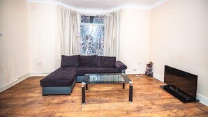 A living room with a sectional sofa, a glass coffee table, and a flat-screen TV. - 6 Bedrooms House NOT FAR from Central London, ECEL LONDON, CANARY WHARF O2 (Barking)