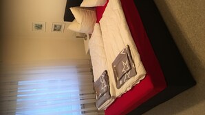 A bedroom with a bed, pillows, and a red accent wall. - An der Bobbahn (Winterberg)