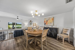 A modern dining area with a round wooden table, six chairs, and a chandelier.