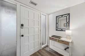 A hallway with a white door, a wall-mounted mirror, and a white console table with a lamp.