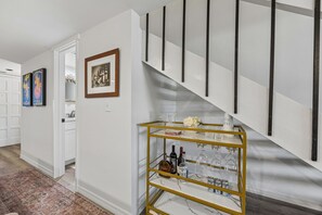 A staircase with a modern design, a white wall with a framed picture, and a gold-framed shelf with bottles and glasses.