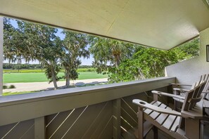 A balcony with a view of a golf course, a wooden chair, and a table.