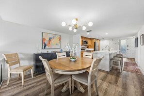 A modern kitchen with a central island, wooden flooring, and a dining area with a round table and chairs.