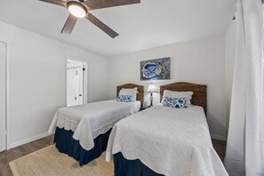 A bedroom with two beds, a ceiling fan, a door, and a painting on the wall.