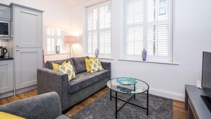 A modern living room with a grey sofa, a glass coffee table, and a TV on a stand. - The Egerton at 52 Old Elvet (Durham)