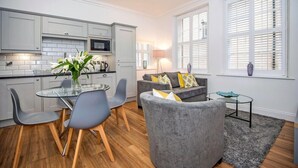 A modern kitchen with grey cabinets, a glass dining table, and a grey sofa in a living area with a view of the outside through large windows. - The Egerton at 52 Old Elvet (Durham)