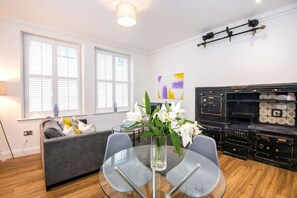 A modern living room with a sofa, a glass table with chairs, a vase of flowers, and a decorative fireplace. - The Egerton at 52 Old Elvet (Durham)