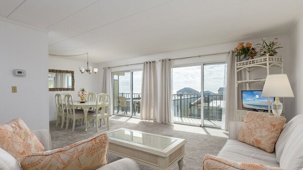 A hotel room with a living area featuring a sofa set, a coffee table, a TV, and a balcony with a view. - Two bedroom mid town with a pool and views! (Ocean City)