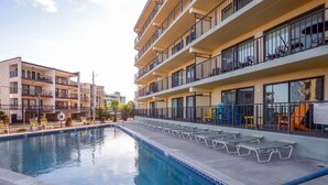 A swimming pool with lounge chairs and a building with multiple balconies. - Two bedroom mid town with a pool and views! (Ocean City)