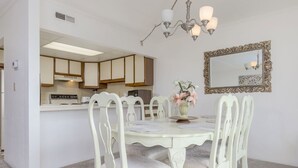A dining area with a white table and chairs, a chandelier, and a mirror on the wall. - Two bedroom mid town with a pool and views! (Ocean City)