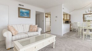 A living room with a white sofa, a glass coffee table, and a dining area with white chairs and a table. - Two bedroom mid town with a pool and views! (Ocean City)