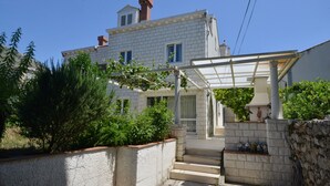 Ein zweistöckiges Haus mit einer Veranda, einer Steinmauer und einem kleinen Garten.