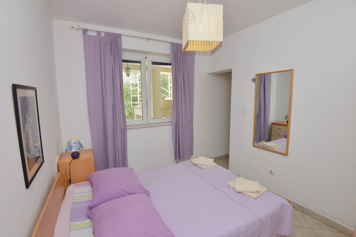 A bedroom with a bed, curtains, a nightstand, a lamp, a mirror, and a window.