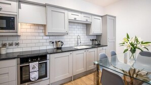 Een moderne keuken met witte kasten, een zwart aanrecht en een glazen eettafel.