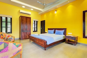 A bedroom with a wooden bed, a nightstand, a chair with a colorful quilt, and a window with blinds. - Oasis of Serenity by Vista Rooms (Luni)