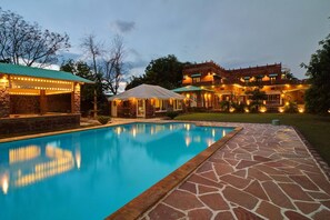 A swimming pool with stone tiles, a stone building with a white roof, and a large brick house with multiple windows and lights. - Oasis of Serenity by Vista Rooms (Luni)