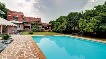 A swimming pool with a stone deck, a brick building with multiple balconies, and lush greenery.