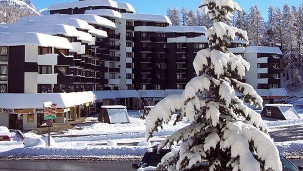A snow-covered building with multiple floors, a parking area, and a snow-laden tree. - Charming Studio Cabin, Sleeps 4, Central Vars - Next to Ski Lifts (Vars)
