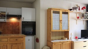 A compact kitchen with wooden cabinets, a built-in oven, and a small refrigerator. - Charming Studio Cabin, Sleeps 4, Central Vars - Next to Ski Lifts (Vars)