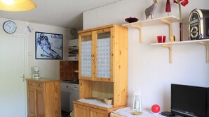 A compact kitchen with wooden cabinets, a stove, and a small dining area. - Charming Studio Cabin, Sleeps 4, Central Vars - Next to Ski Lifts (Vars)