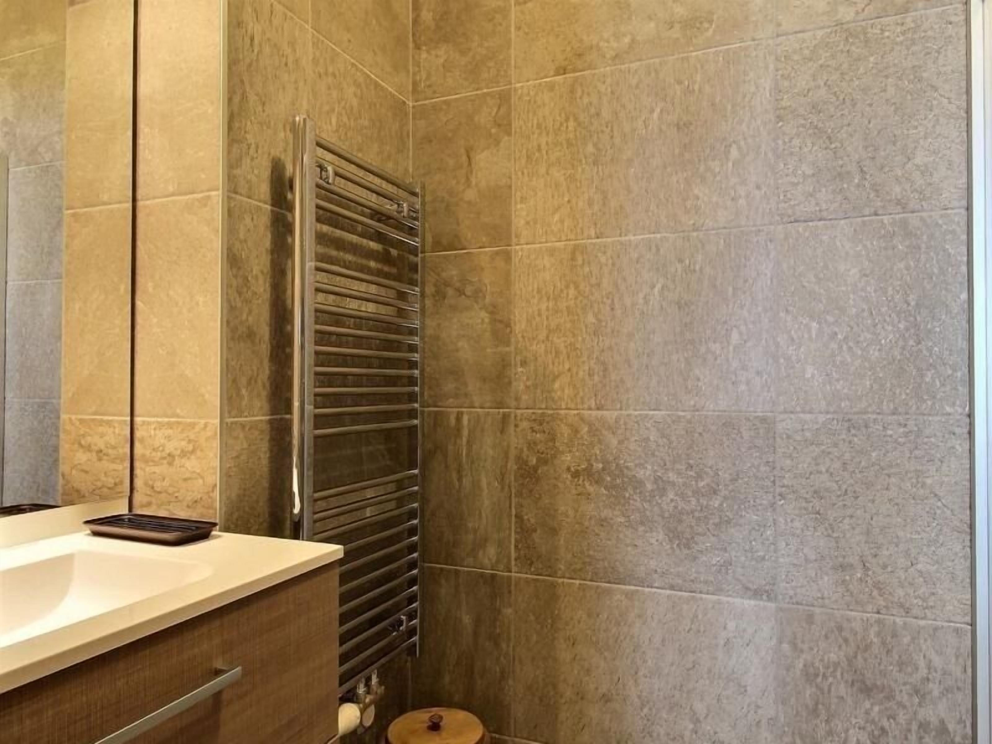 A bathroom with a modern design, featuring a large mirror, a towel rack, and a sink with a countertop.