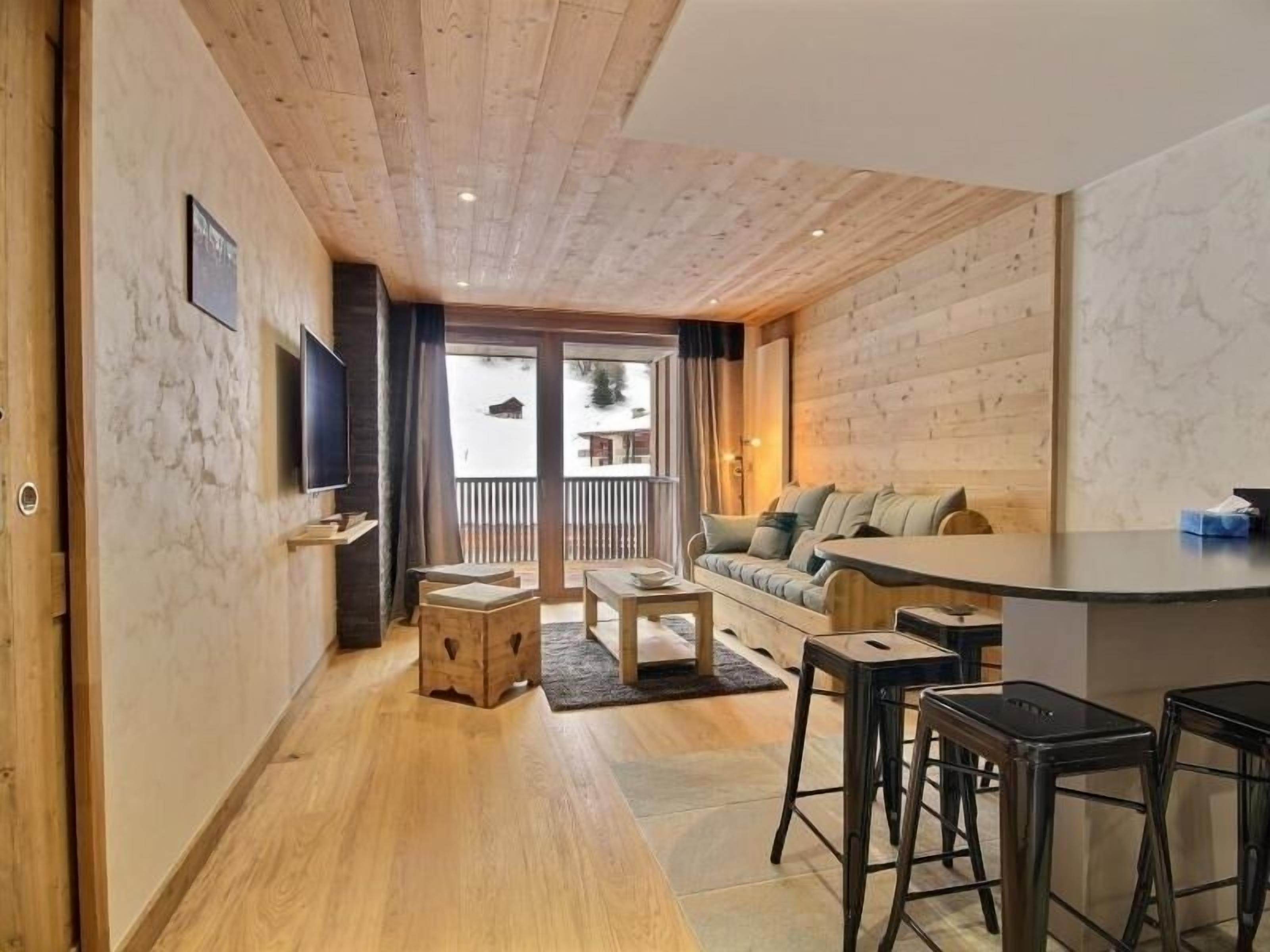 A cozy living area with a wooden ceiling, a sofa, a coffee table, and a TV mounted on the wall.