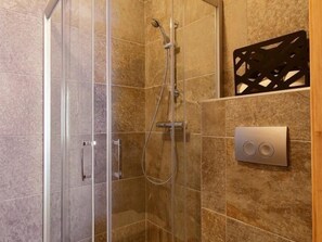 Ducha moderna con cabina de vidrio, cabezal de ducha de mano y panel de control con dos botones.