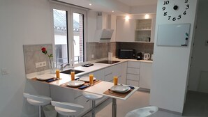 A modern kitchen with a central island, bar stools, a microwave, and a whiteboard with a clock. - ecoSmart Apartments Superior (Granada)