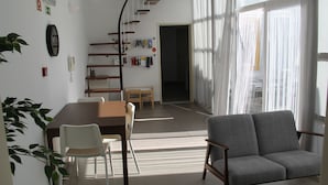 A modern living room with a sofa, dining table, chairs, a staircase, and a large window with curtains. - StayInn City - Évora (Évora)