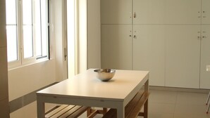 A modern kitchen with a white table, wooden bench, pendant lighting, and cabinets. - StayInn City - Évora (Évora)