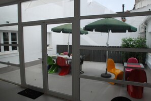 A glass-enclosed patio area with colorful chairs and umbrellas, a table, and a view of the outside.