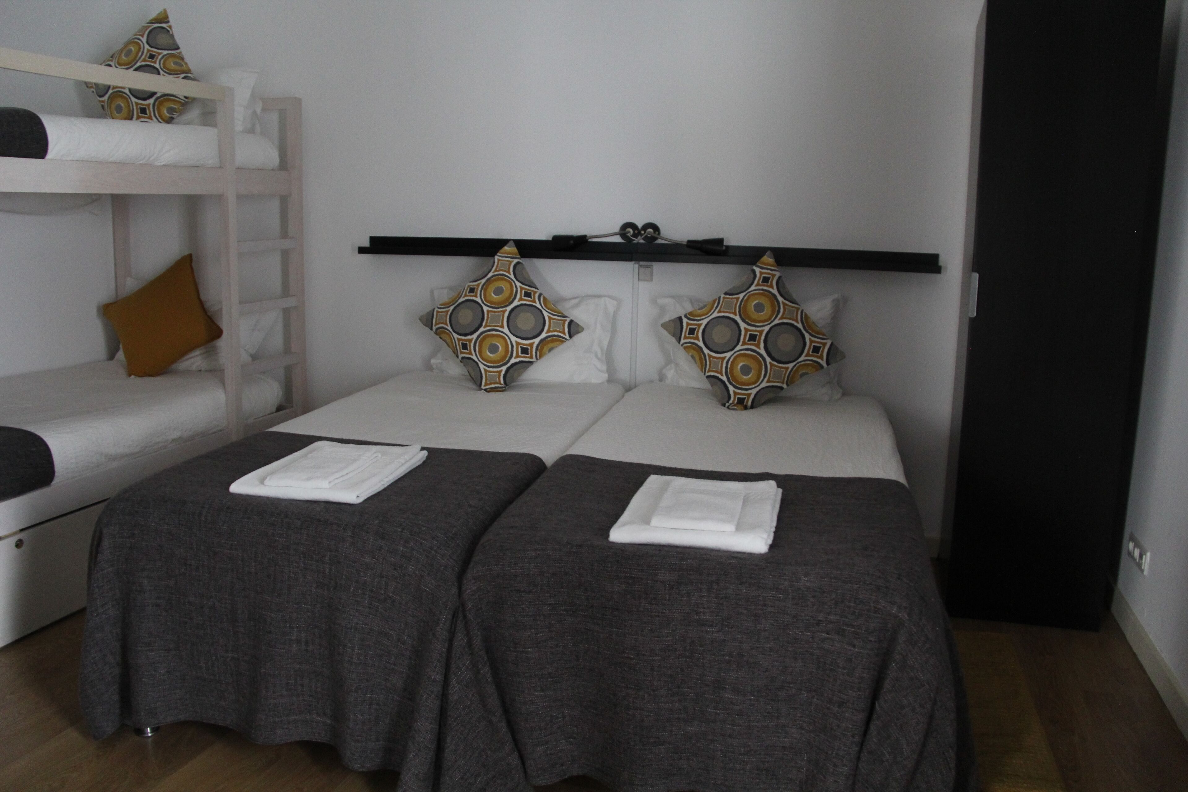 Quarto com duas camas de solteiro, uma cama beliche e uma prateleira sobre as camas.